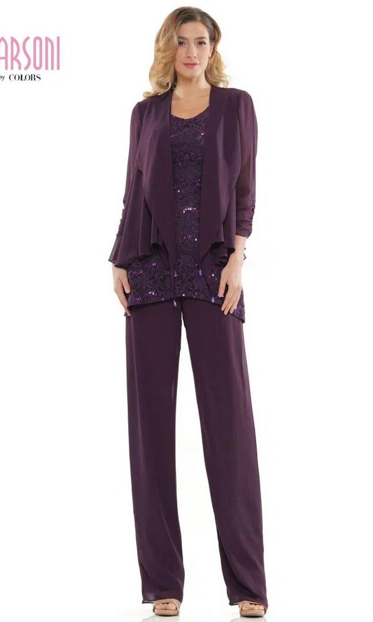 A woman stands wearing the Marsoni M303 long formal pantsuit in eggplant, featuring a chiffon jacket, wide-leg pants, and a sequined sleeveless lace top.